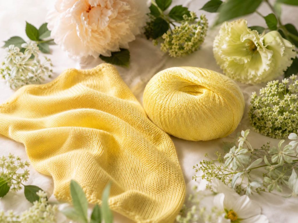 Et smukt fint gul garn der ligger på hvidt stof omgivet af blomster